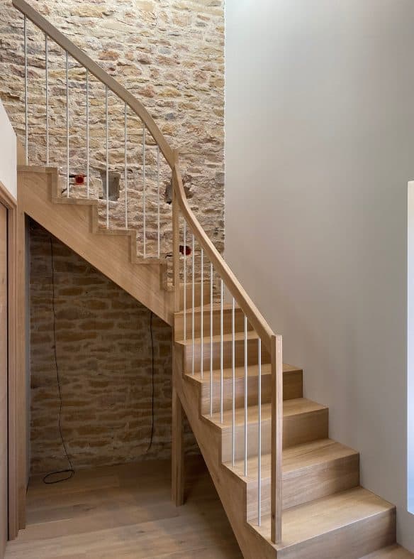 Escalier quart tournant en chêne, barreaux métal blancs, mur en pierre