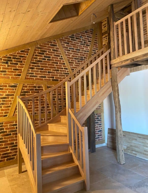 Escalier quart tournant en hêtre devant un mur de briques et de colombages